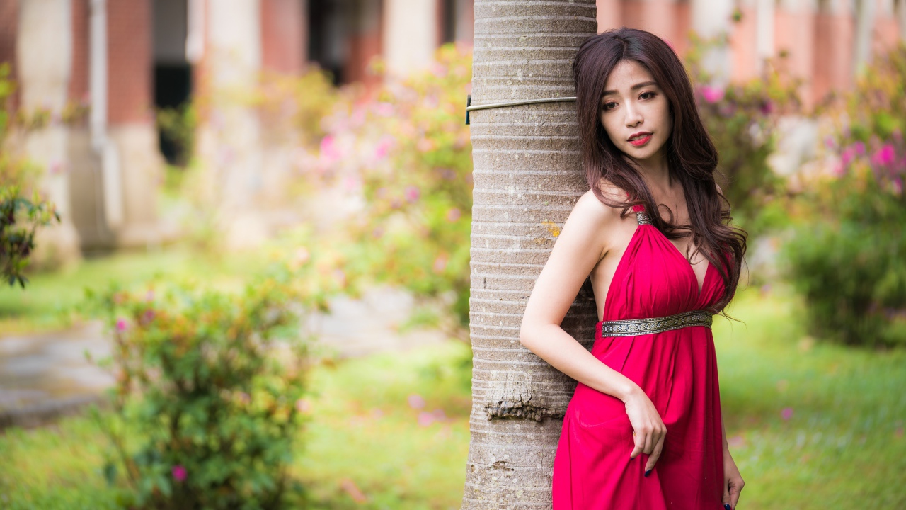 Стройная азиатка в красном платье у дерева 
