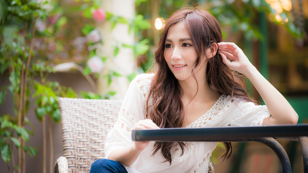 Улыбающаяся девушка азиатка сидит за столом в кафе