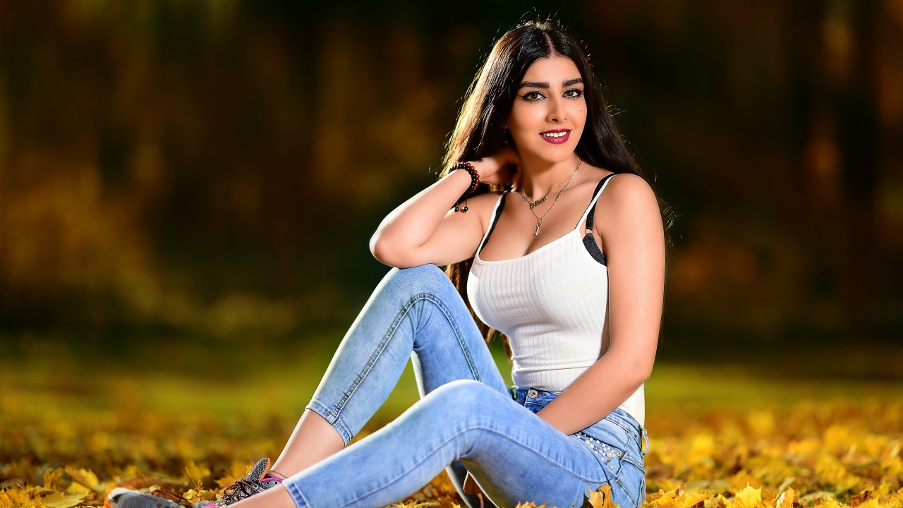 Улыбающаяся брюнетка сидит на опавшей листве