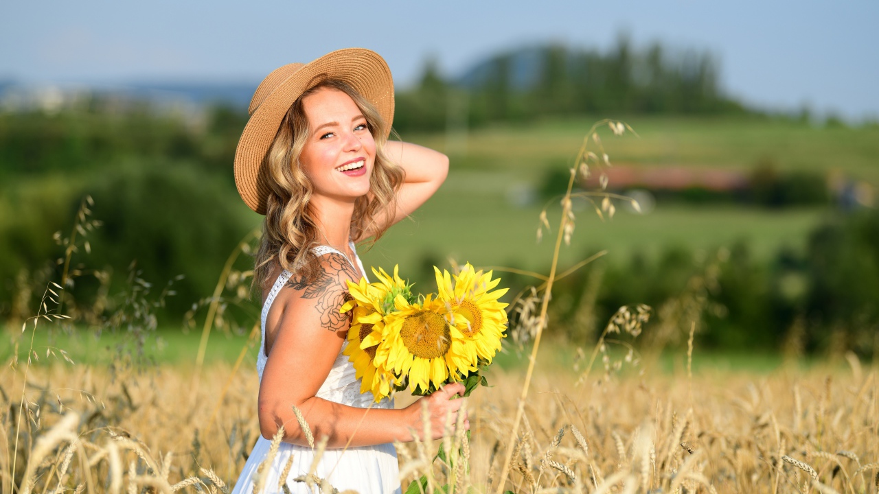 Улыбающаяся девушка с букетом подсолнухов на поле пшеницы
