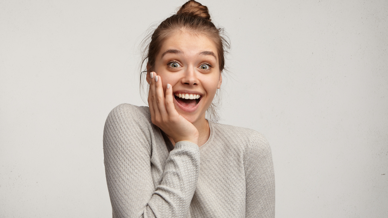 Удивленная девушка с рукой у лица на сером фоне 