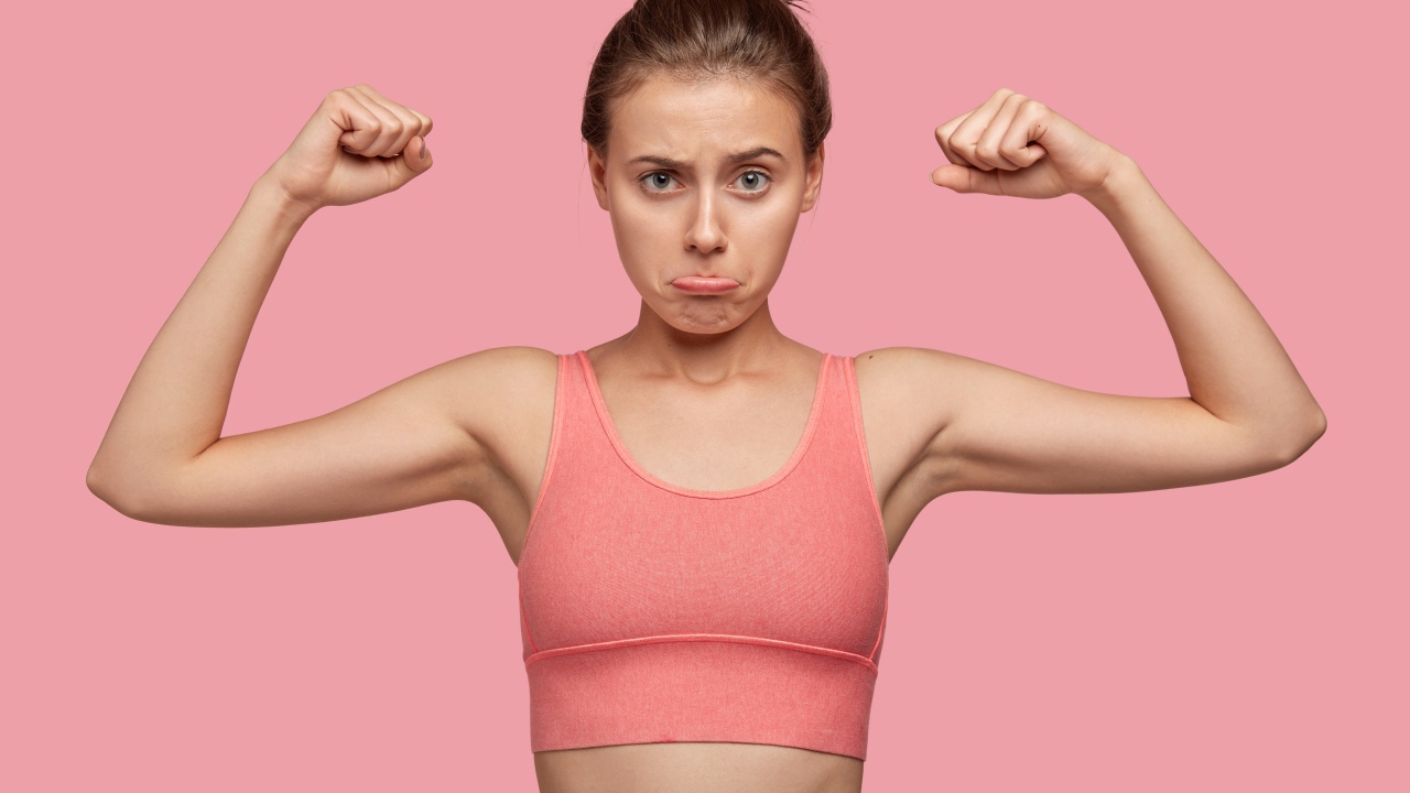 Расстроенная девушка без накаченных рук на розовом фоне