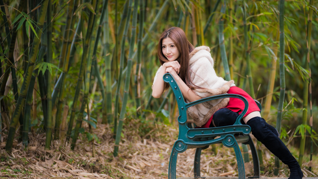 Молодая девушка азиатка сидит на зеленой лавке 