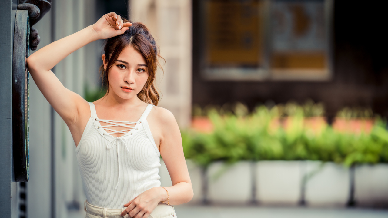 Молодая красивая азиатка в белой майке стоит у ворот