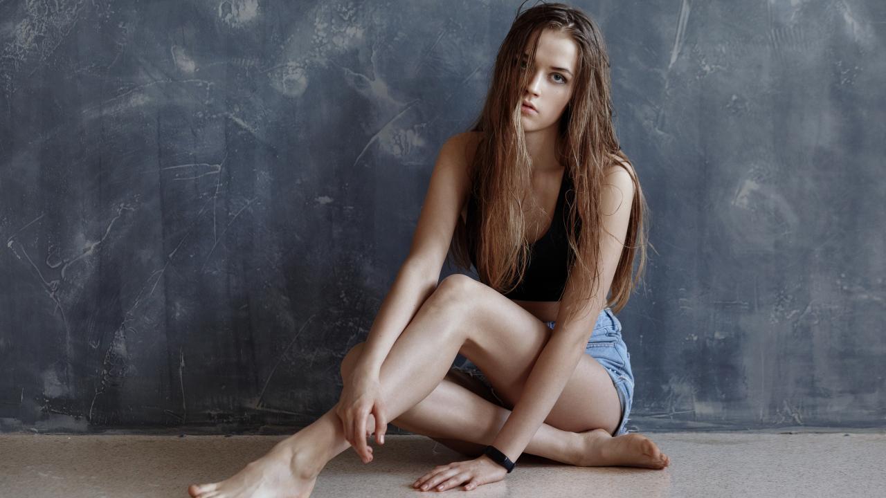 Молодая девушка с мокрыми волосами сидит у стены 