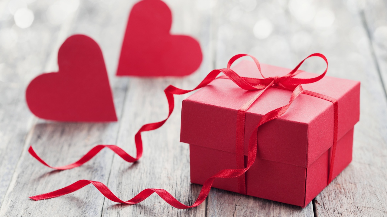 Красная коробка с подарком на столе с красными сердечками