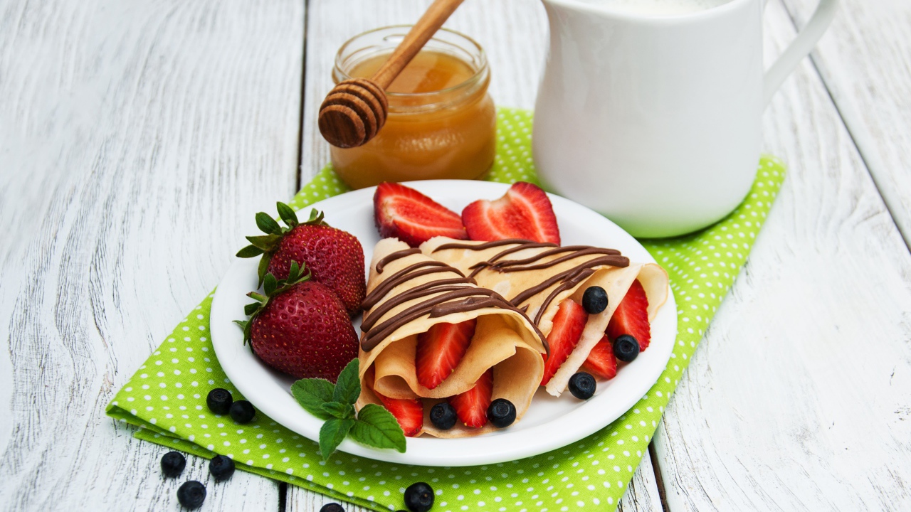 Вкусные блины с клубникой на столе с молоком и медом на праздник Масленица