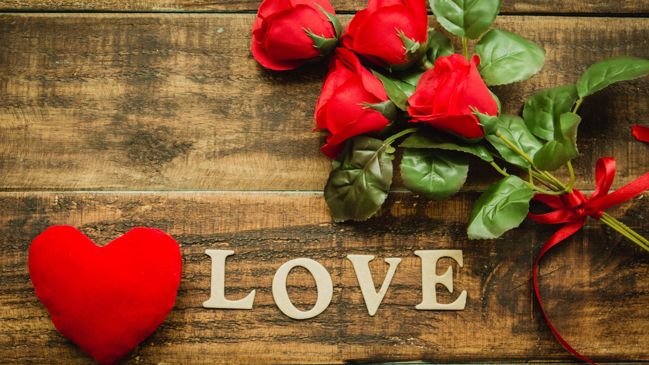 Надпись LOVE на столе с розами и красным сердцем