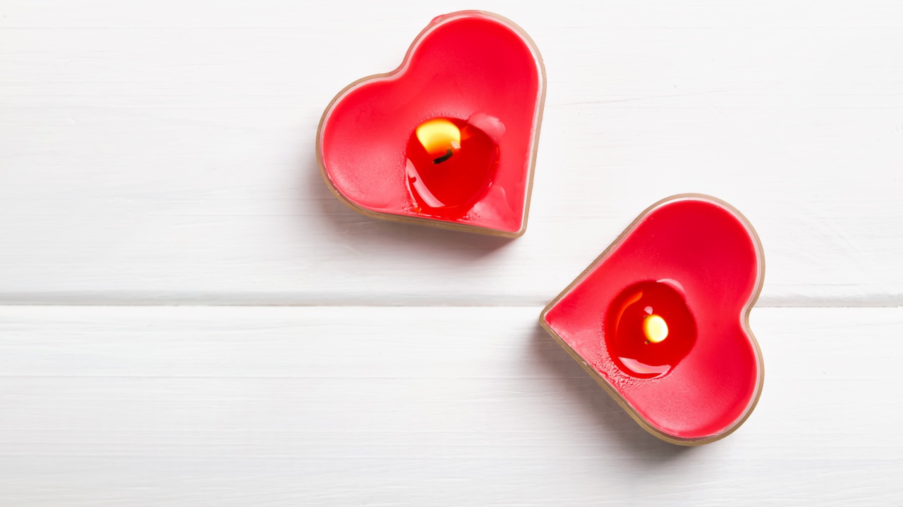 Two burning candles in the shape of a heart on the table