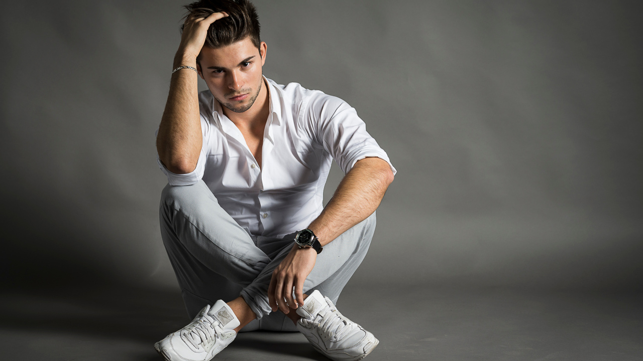 Красивый молодой человек в белой рубашке сидит у стены 