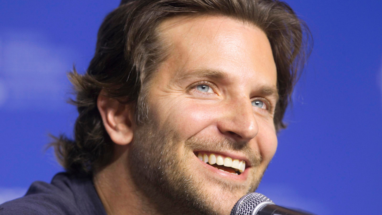 Голубоглазый актер Брэдли Купер с микрофоном на синем фоне