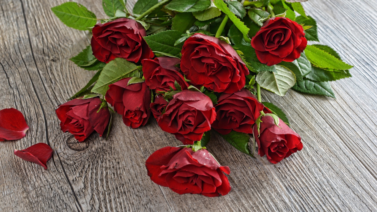 Красивый букет алых роз с зелеными листьями на деревянном столе