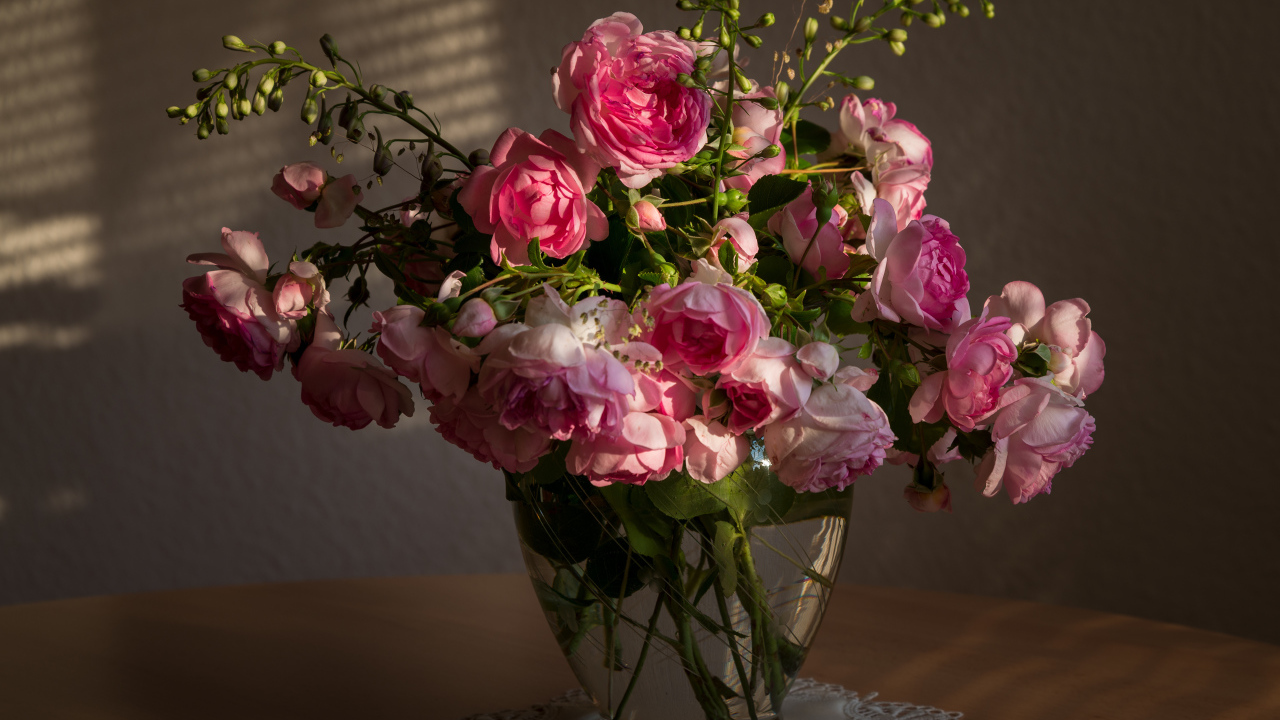 Букет розовых роз в стеклянной вазе не столе в лучах солнца 