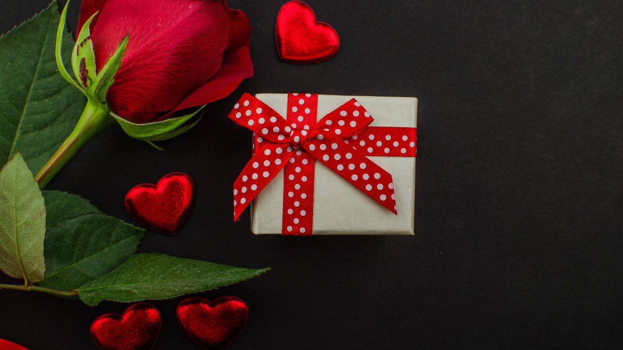 Маленький подарок и красная роза на черном столе