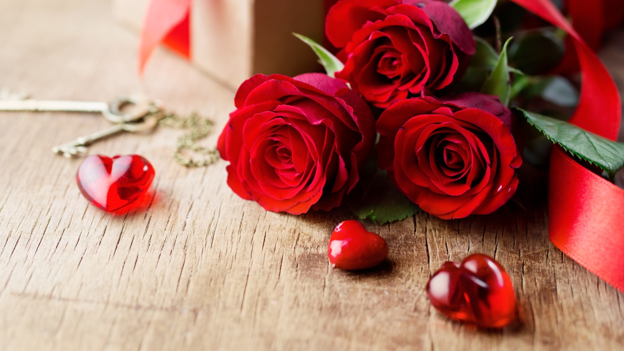 Три красивые красные розы на столе с сердечками и ключами