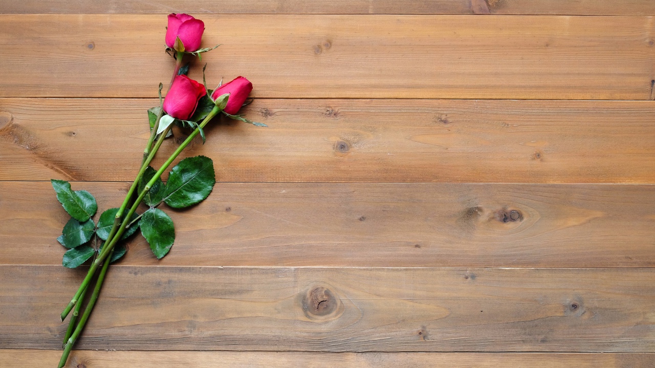 Три красные розы лежат на деревянном столе 