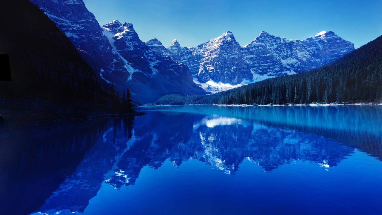 Высокие заснеженные горы отражаются в воде озера 