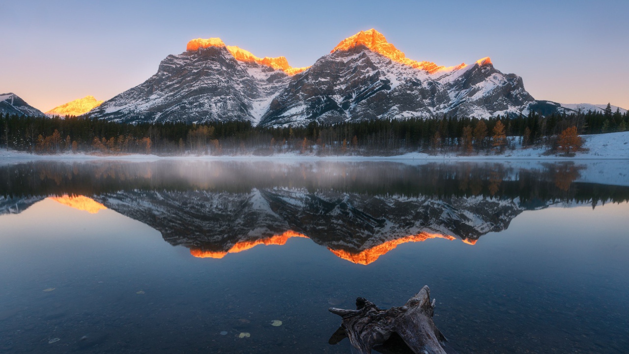 Вершины гор в лучах солнца отражаются в чистой воде озера