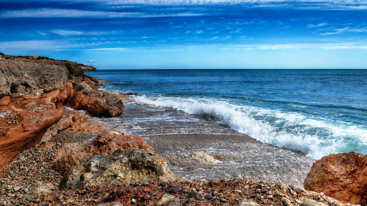 Белые волны на берегу моря с большими камнями под голубым небом