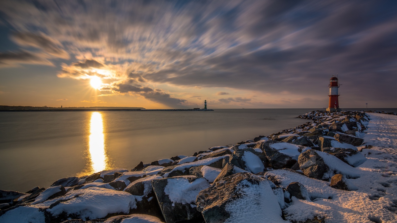Заснеженные камни на берегу моря с маяком на закате