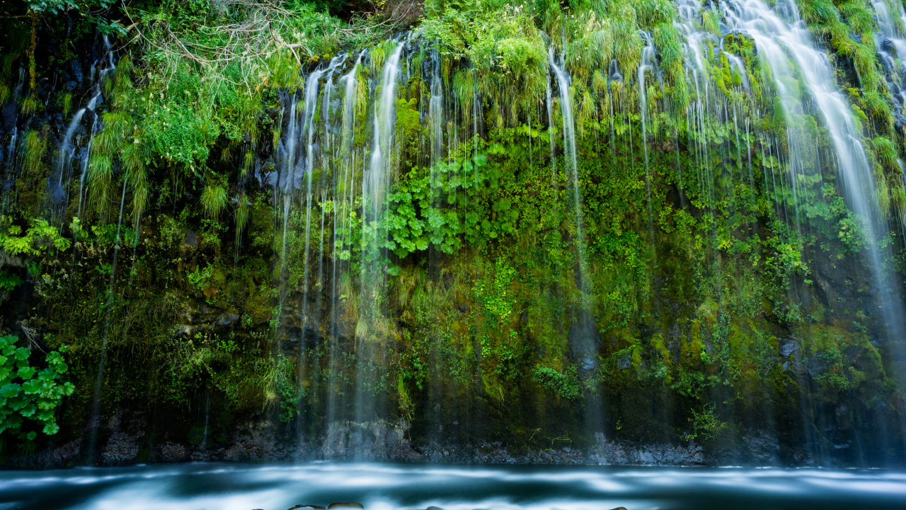 Красивый водопад стекает по покрытом зеленью утесе 