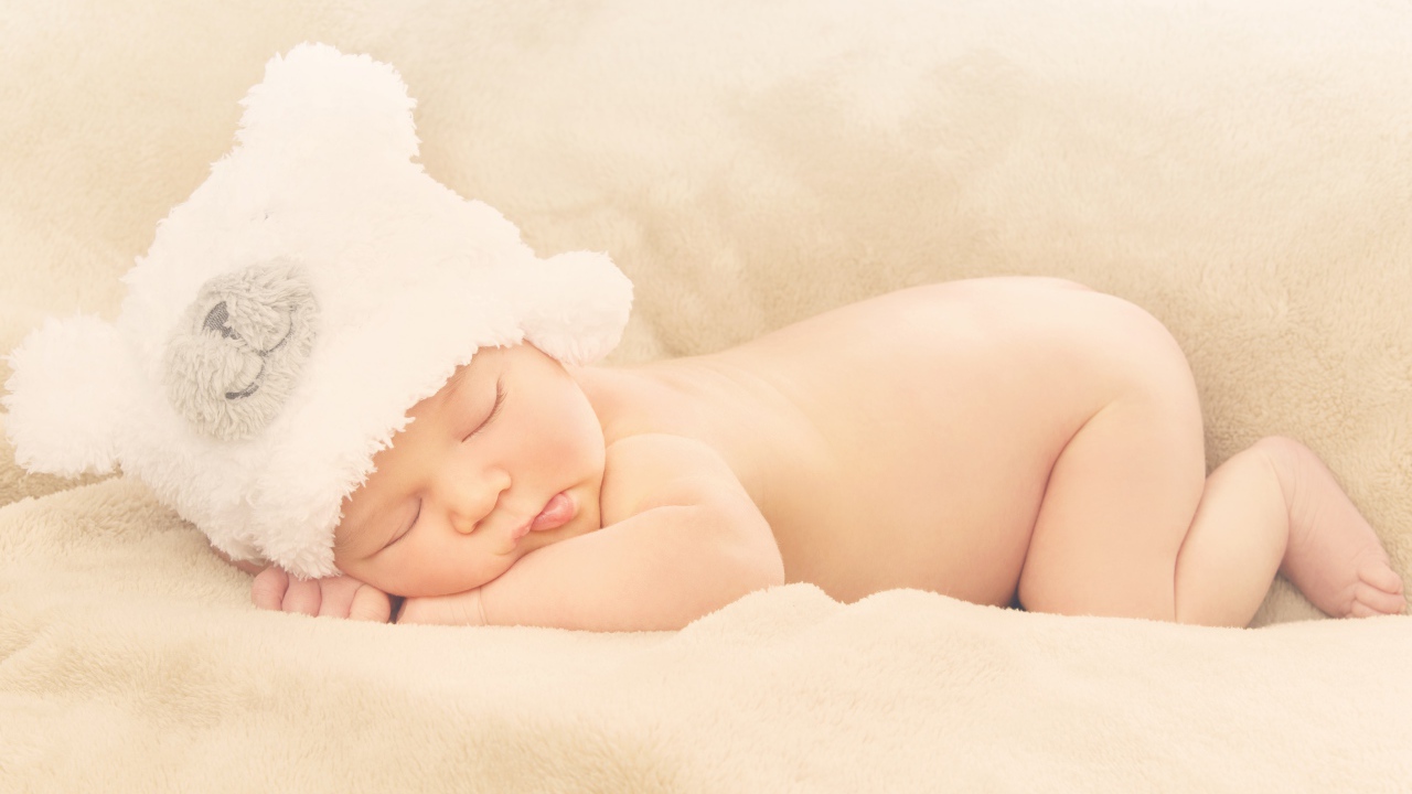 Грудной ребенок с белой шапке спит на кровати