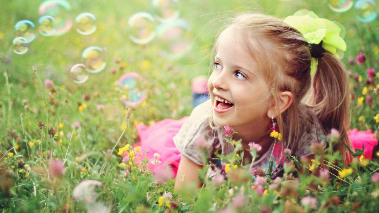 Веселая девочка лежит на траве с мыльными пузырями