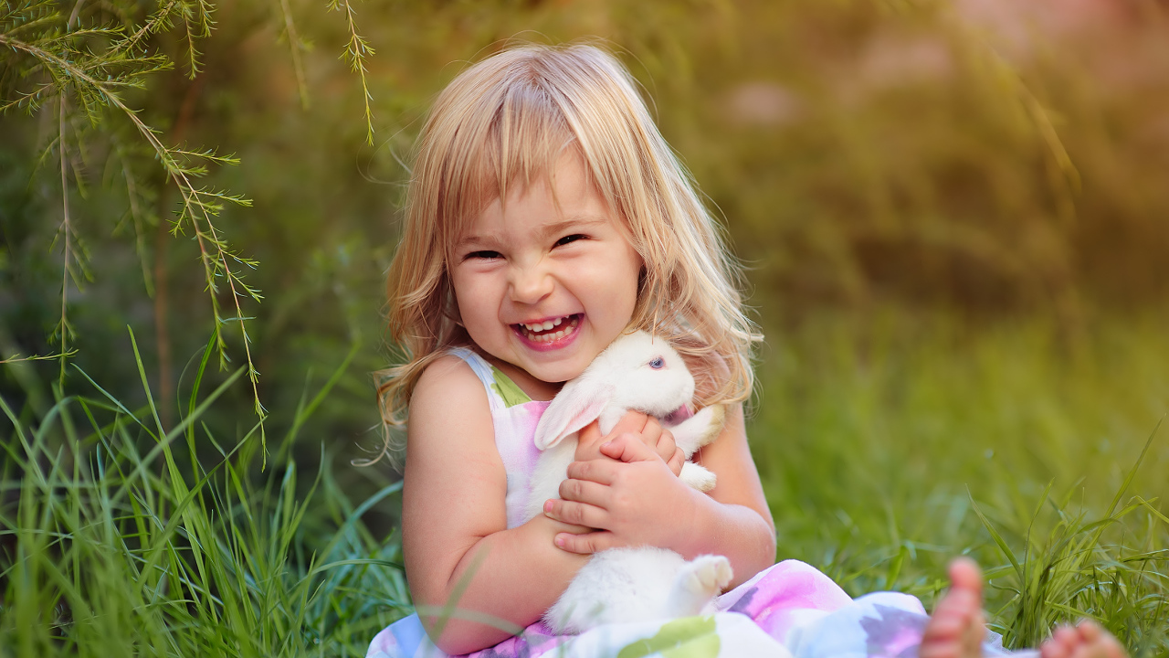 Довольная маленькая девочка обнимает белого кролика на траве 