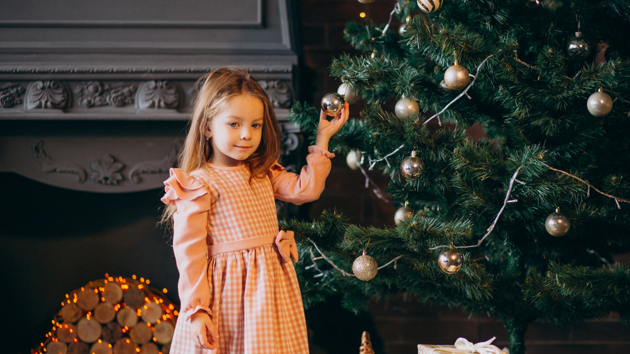 Милая маленькая девочка стоит у наряженной елки 