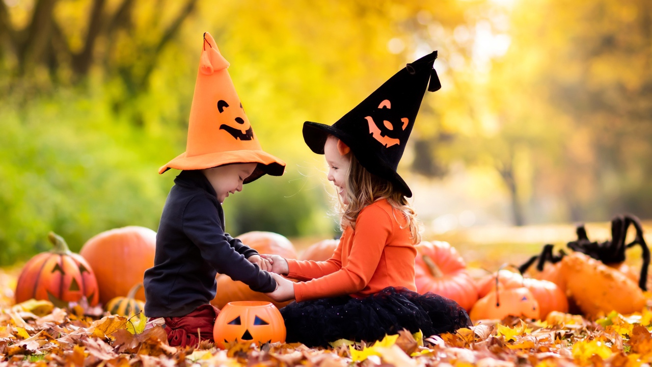 Маленькие мальчик и девочка в костюмах на Хэллоуин сидят на листве