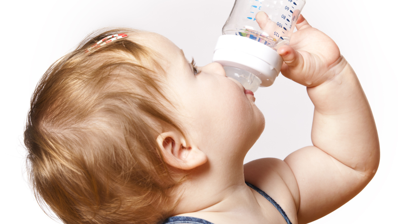 Маленькая девочка пьет молоко с бутылочки на белом фоне