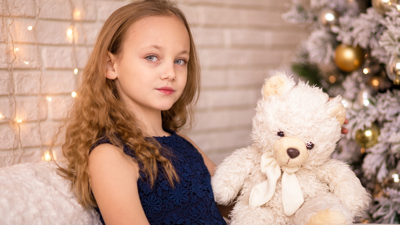 Маленькая девочка с мишкой сидит у наряженной ели 