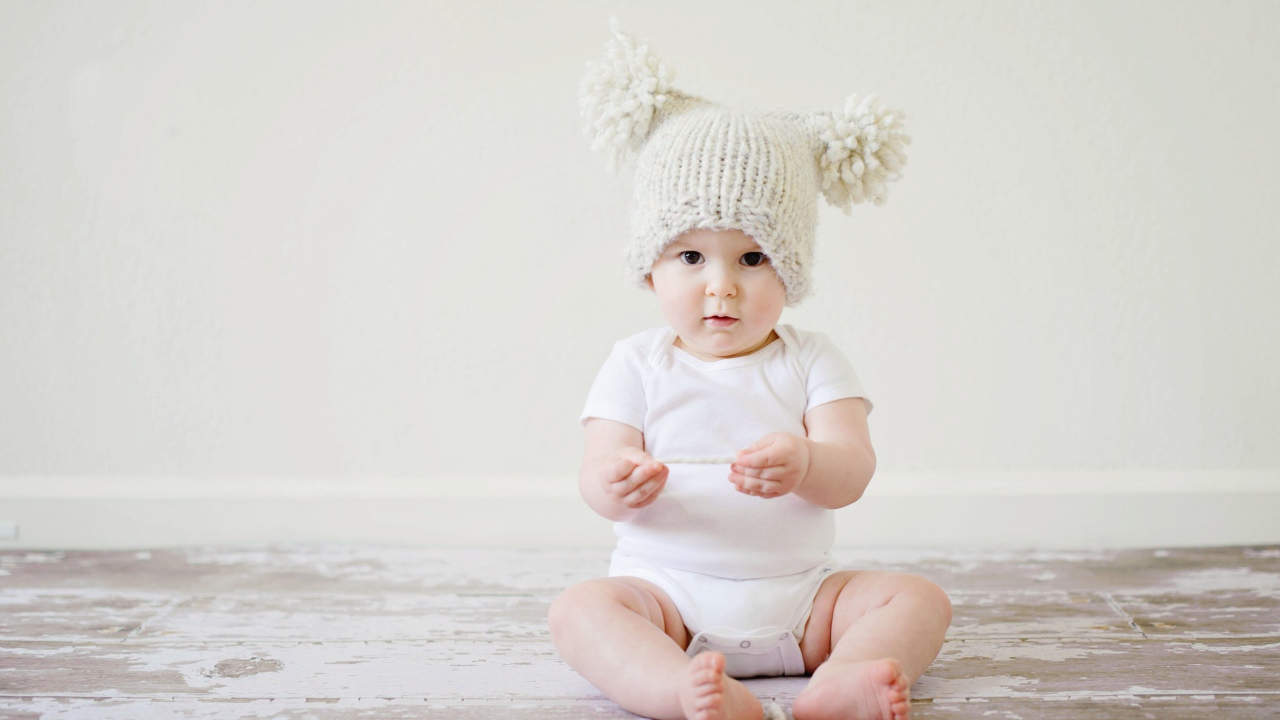 Маленький грудной ребенок в боди с шапкой на голове