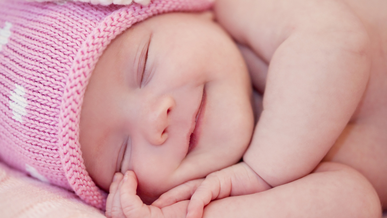 Улыбающийся грудной ребенок в розовой вязаной шапке 