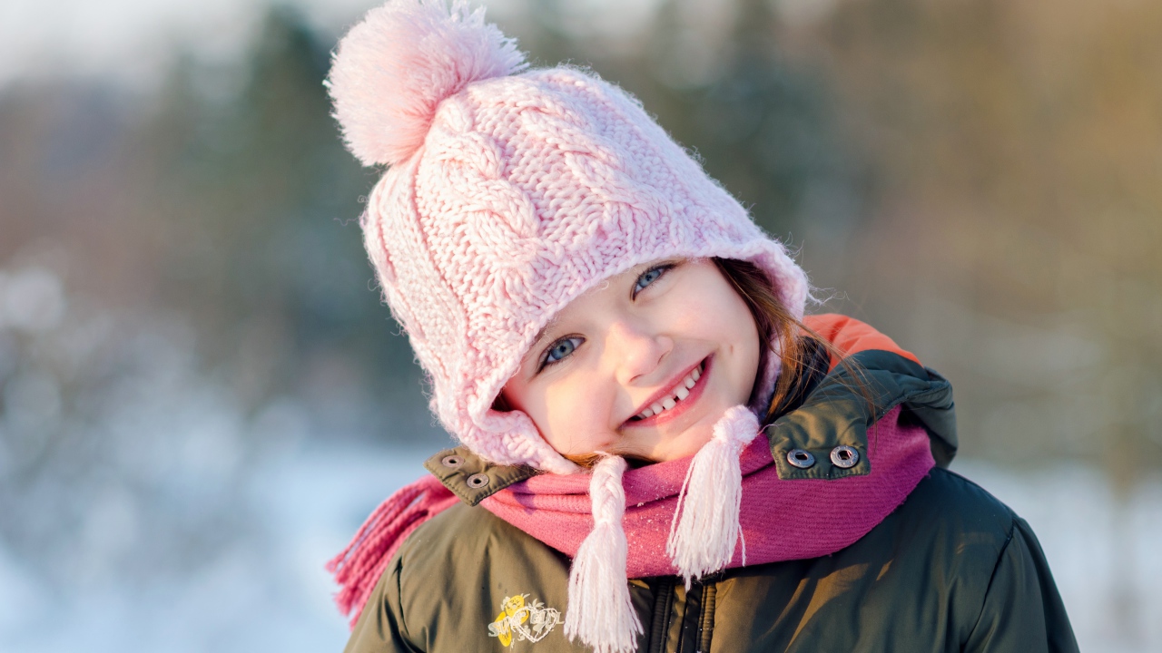 Улыбающаяся девочка в розовой шапке зимой