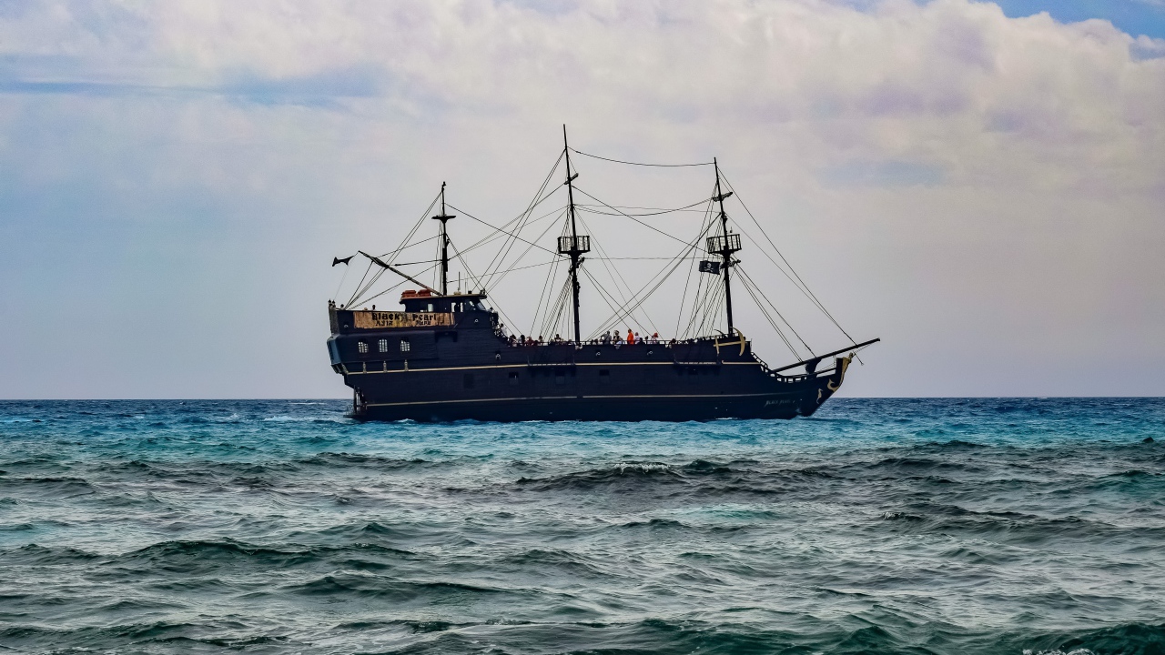 Большой черный пиратский корабль с опущенными парусами в море 