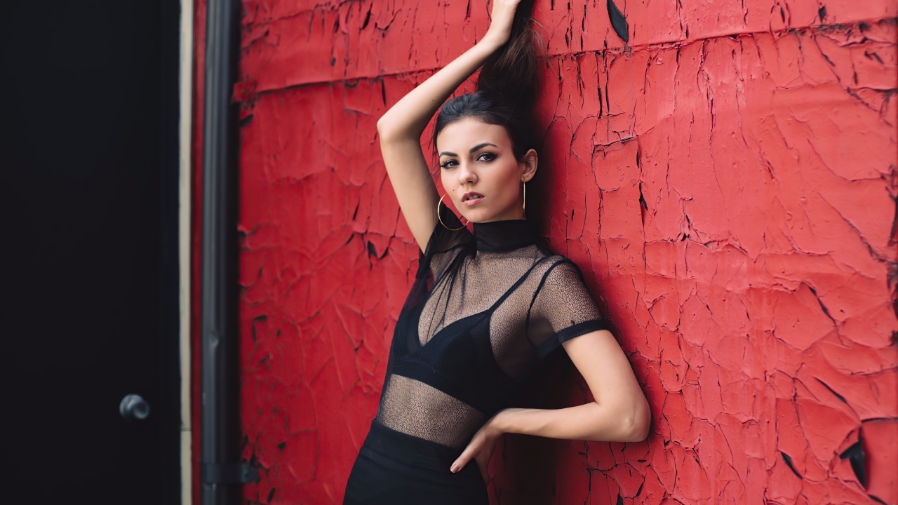 Актриса Виктория Джастис в черном наряде на фоне красной стены