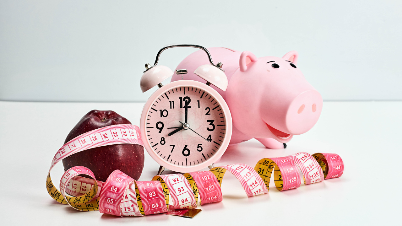 Будильник, свинья копилка, яблоко и сантиметр на белом фоне