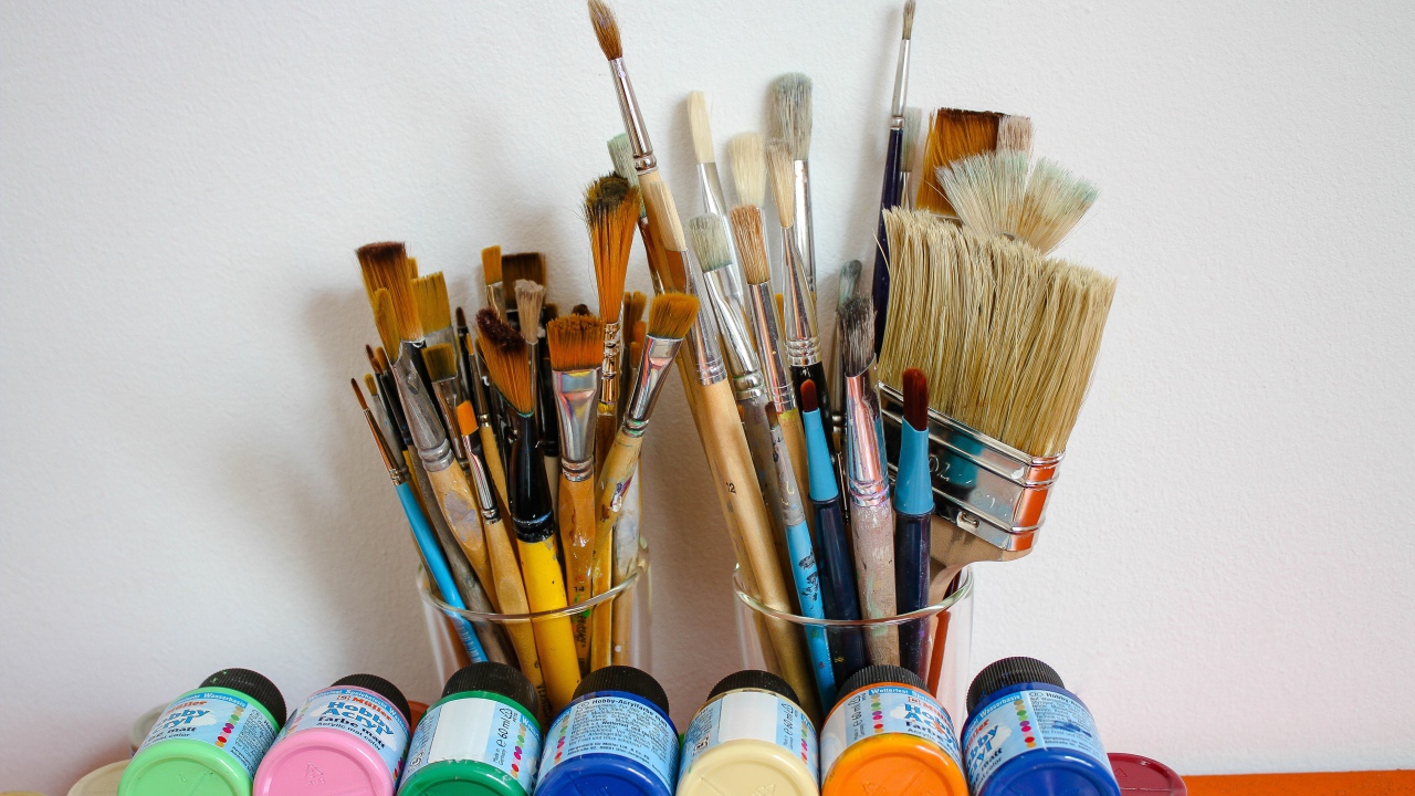 Много кисточек и разноцветные краски у стены