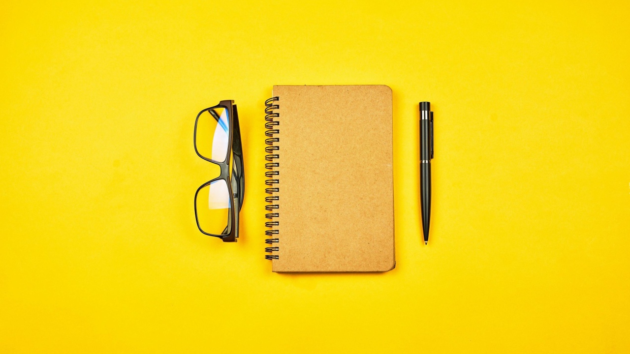 Notepad, glasses and pen on yellow background