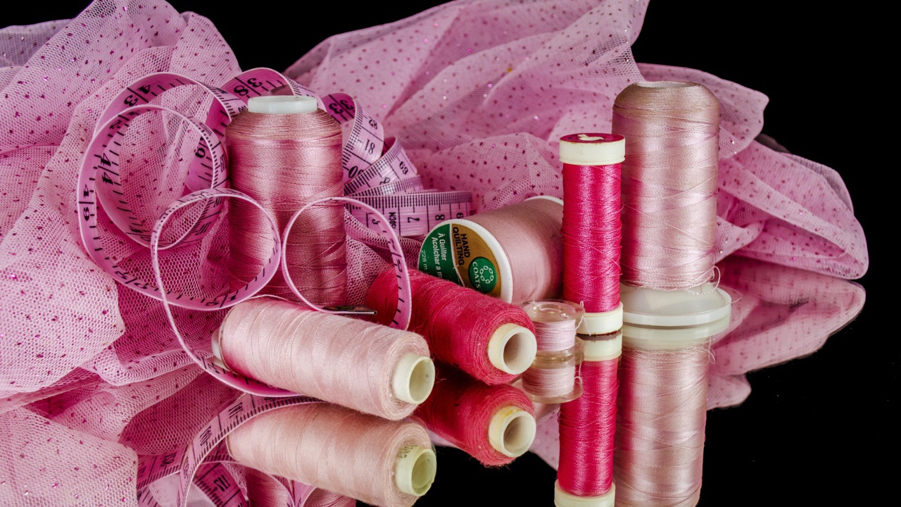 Розовые нитки с сантиметром и тканью на черном фоне 