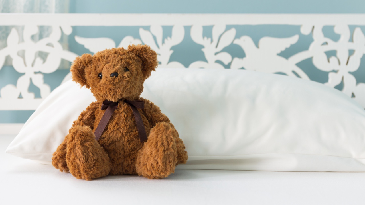 Игрушечный медвежонок сидит на белой постели