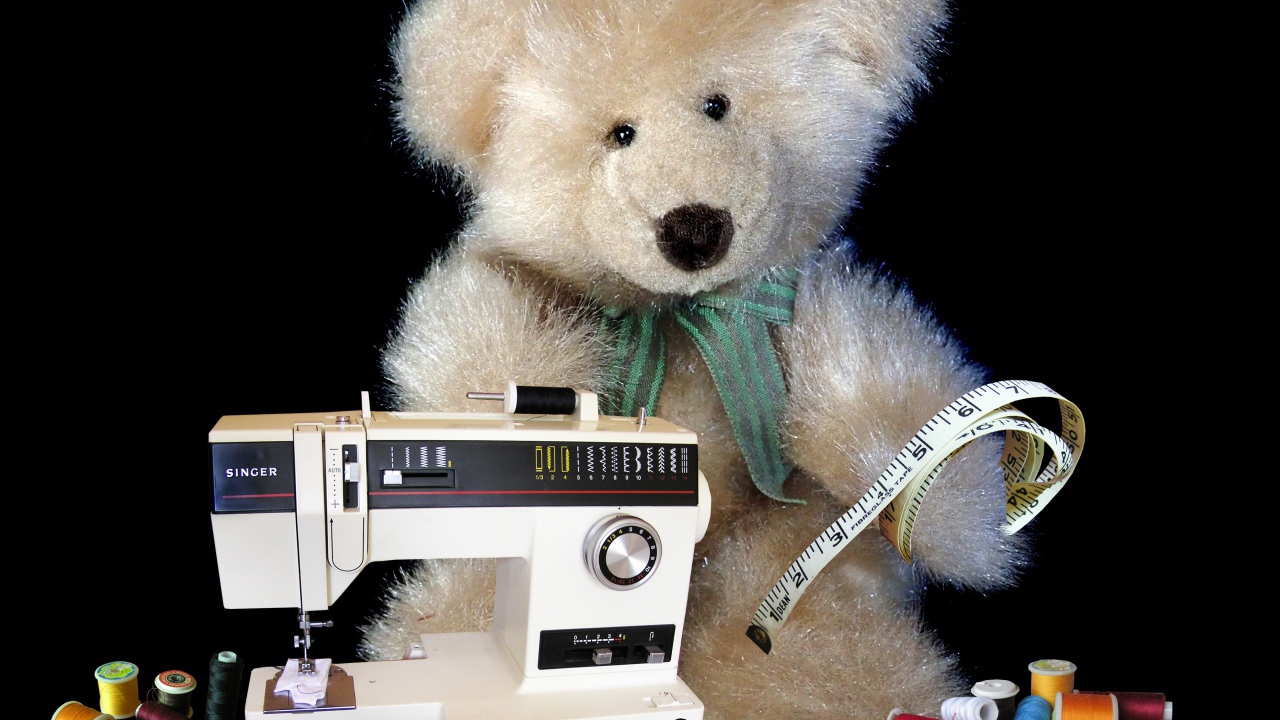 Игрушечный медвежонок со швейной машинкой на черном фоне 