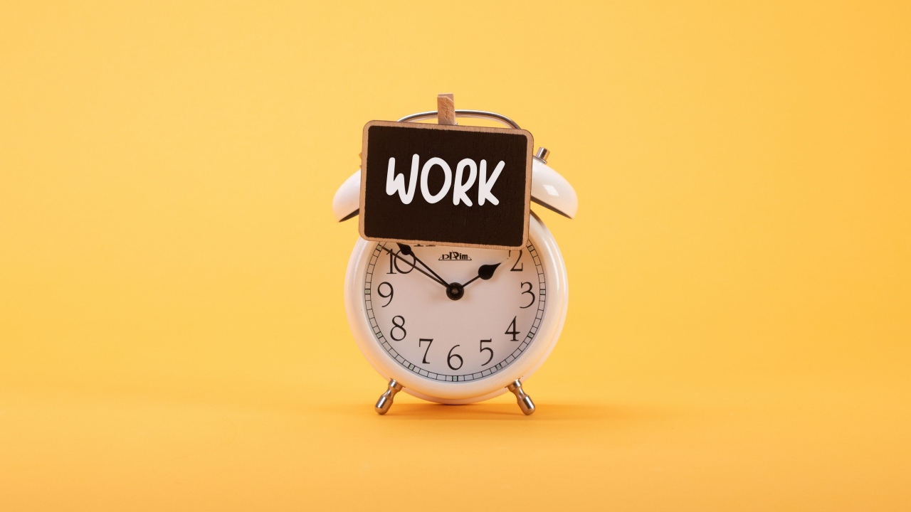 Белый будильник с табличкой на желтом фоне