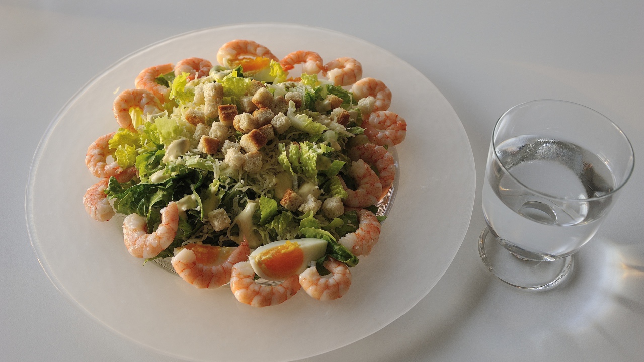 Тарелка аппетитного салата с креветками на столе с рюмкой