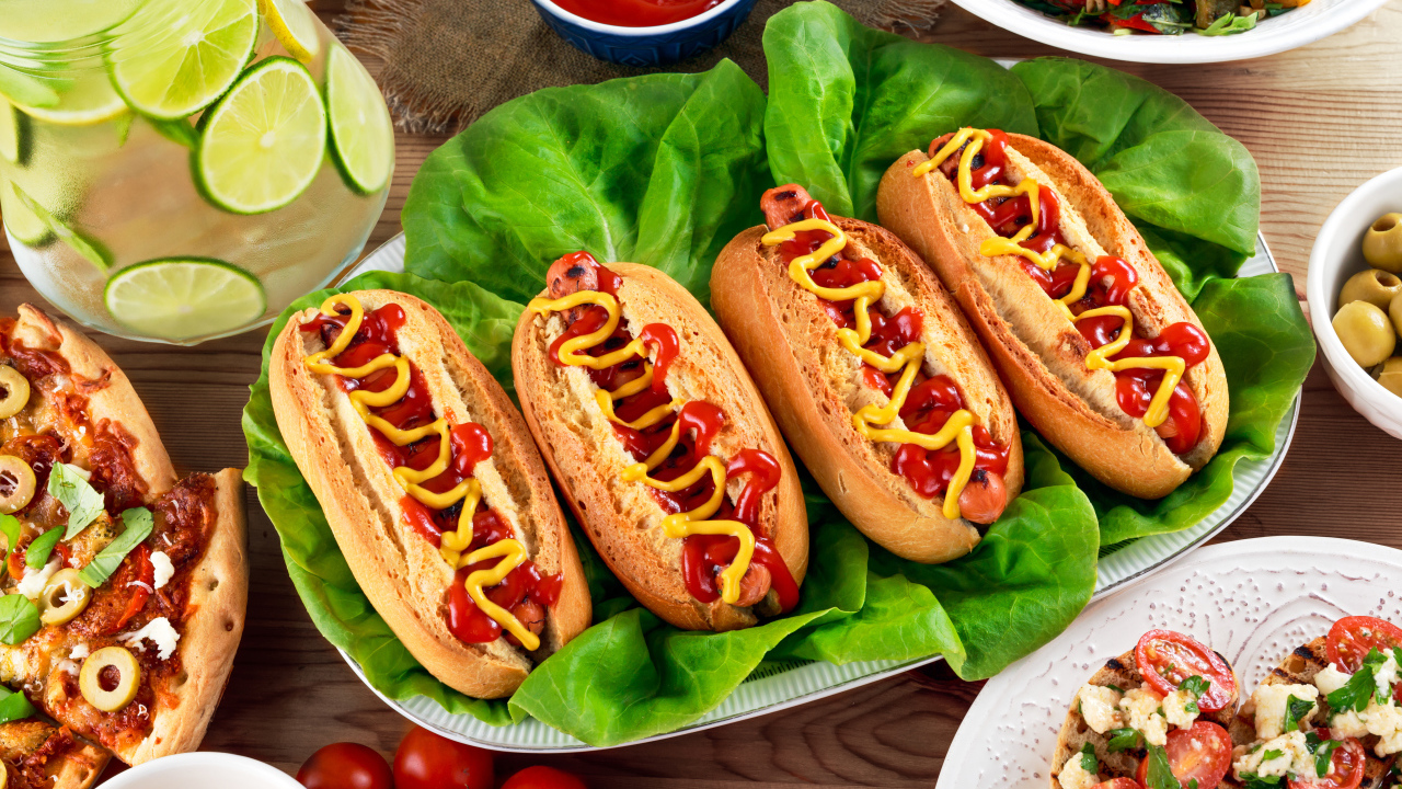 Хотдоги, пицца, лимонад и салат на столе