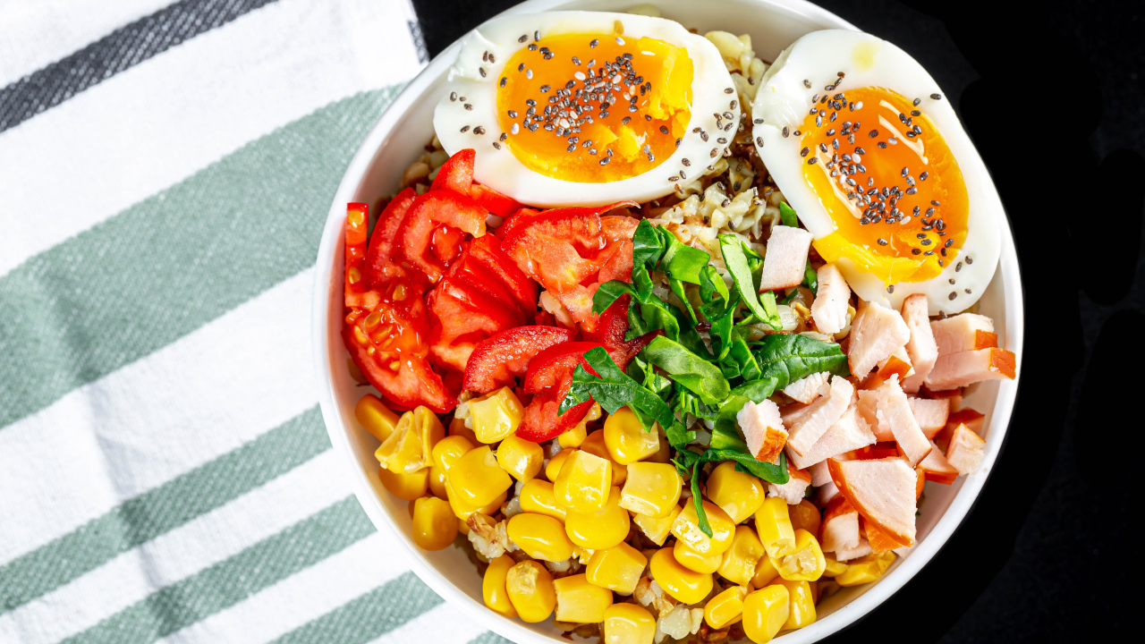 Каша в тарелке с помидорами, кукурузой, ветчиной и яйцом