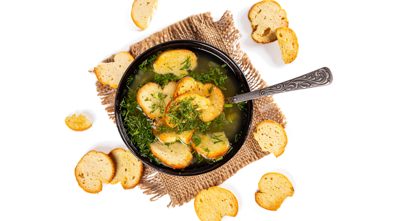 Суп с гренками и зеленью на столе на белом фоне