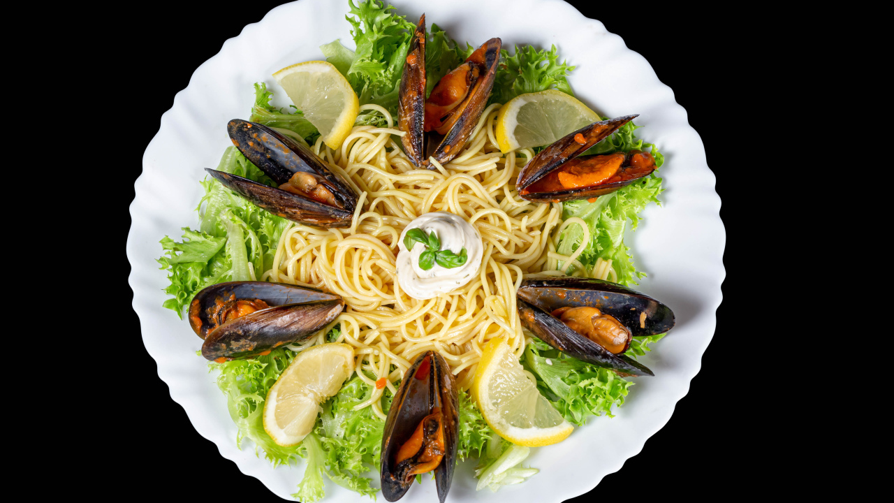 Спагетти с мидиями и листьями салата на белой тарелке