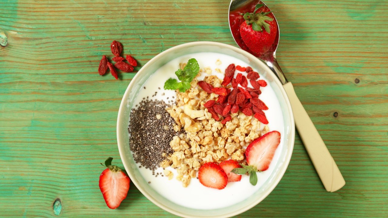 Йогурт с сухофруктами и клубникой на столе в миске 